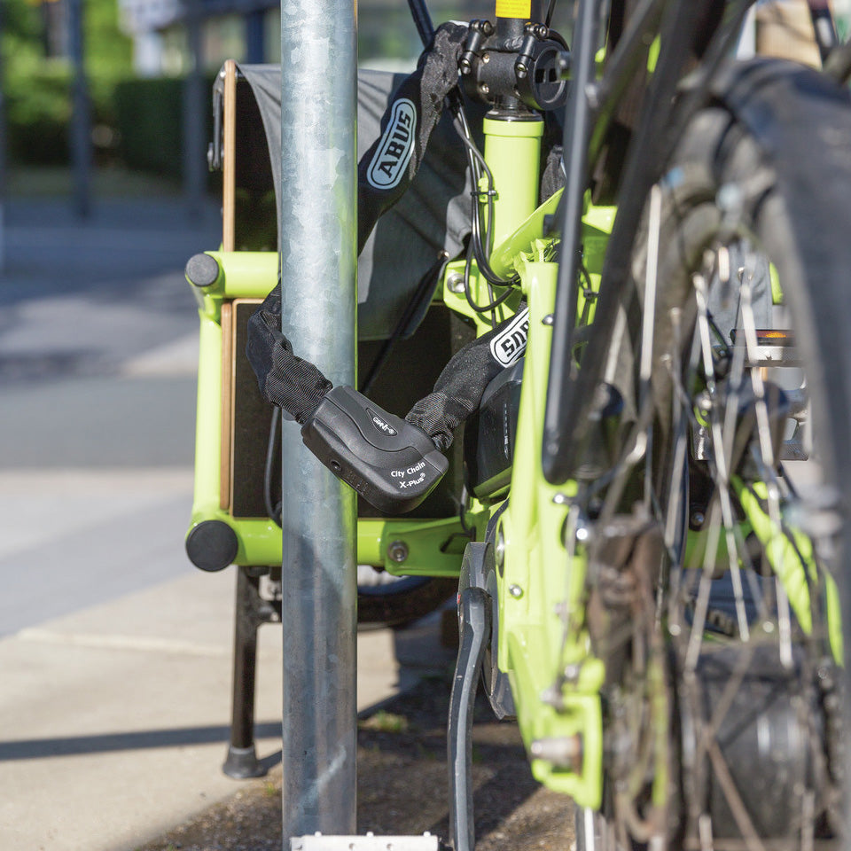 ABUS GRANIT CityChain XPlus™ lock securing a bicycle to a metal post, showcasing its heavy-duty hexagonal chain and reinforced lock body.